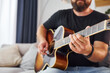 © standret - Playing the instrument. Man in casual clothes and with acoustic guitar is indoors