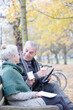 © KOTO - Senior couple reading newspaper and drinking coffee on bench in autumn park