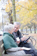 © KOTO - Senior couple reading newspaper and drinking coffee on bench in autumn park
