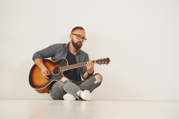 In the studio. Man in casual clothes and with acoustic guitar is indoors