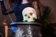 Close-up, focus on a human skull in the hands of a witch over a black cauldron in a dark room.