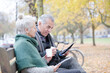 © KOTO - Senior couple reading newspaper and drinking coffee on bench in autumn park