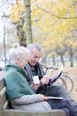 Wall Mural - Senior couple reading newspaper and drinking coffee on bench in autumn park