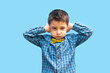 the little boy covered his ears with his hands. children's whims. portrait of a boy on a blue background