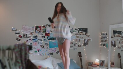 happy teenage girl dancing on bed at home to music enjoying celebrating weekend having fun singing w