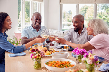 Senior Parents With Adult Offspring Making Toast Sitting Around Table For Family Meal