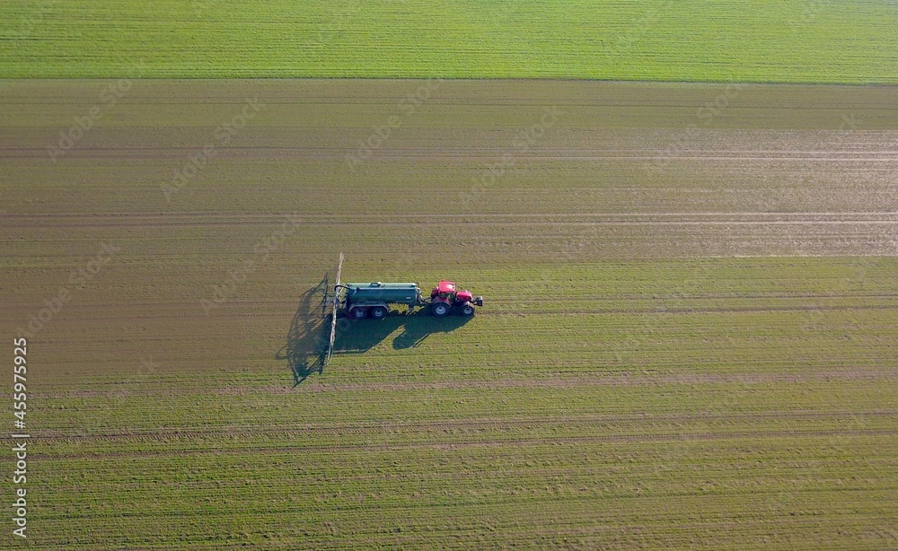 Industrial agriculture: tractor with slurry tanker spreads slurry on fields, bird's eye view