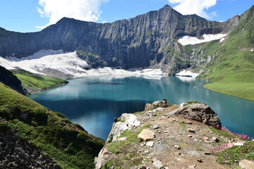 Canvas Print - Breathtaking view of snowy rocks with green hills and blue lake