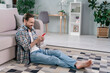 © deagreez - Profile side view portrait of attractive cheerful guy sitting on carpet using device wi fi at light room indoors