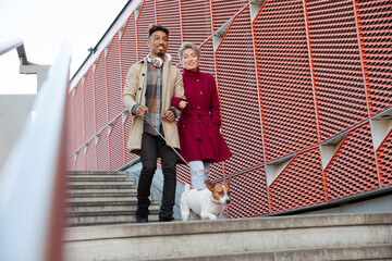 Smiling young couple walking dog down urban, modern stairs