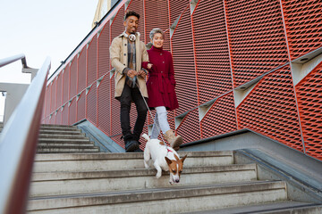 Wall Mural - Smiling young couple walking dog down urban, modern stairs