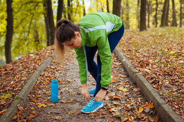 Runner tying shoe laces in autumn park. Woman training with water bottle. Active healthy sportive lifestyle