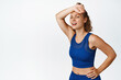 © Cookie Studio - Fitness woman finish running exercises, wipe sweat on forehead with arm, heavy breathing after jogging. Concept of workout and sport, standing against white background