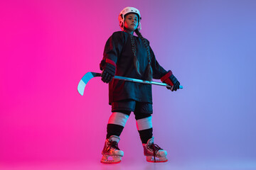 Wall Mural - Full-length portrait of child playing professional hockey isolated over gradient pink purple background