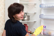 © ALEXEY - A woman washes the internal shelves of the refrigerator in yellow rubber gloves, cleaning the apartment.