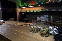 Jars Of Dried Marijuana Flower Buds On Table In Workspace