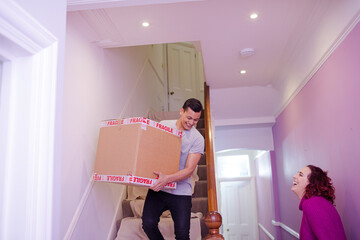 Wall Mural - Happy couple moving out of house, carrying cardboard box down stairs