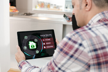 Man setting smart home alarm system from digital tablet on living room sofa