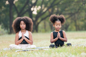 two african american little girl doing meditate yoga asana on roll mat with eyes closed in park. kid