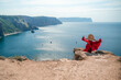 © svetograph - A girl with loose hair in a long red dress descends the stairs between the yellow rocks overlooking the sea. A rock can be seen in the sea. Sunny path on the sea from the rising sun