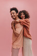 profile photo of young woman hugging from behind tall guy indoors in pink. happy brunettes with curly hair are dressed in light summer clothes.