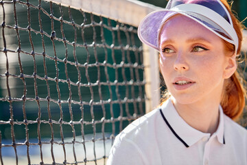 Wall Mural - young fit redhead woman outdoor on orange tennis field at early morning, came to play. confident pretty lady in white tennis uniform looking at side, standing next to net. portrait.tennis concept