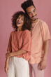 © Look! - cheerful African friends are leaning against each other in light studio. young woman with open smile in coral t-shirt and white pants. man in peach T-shirt and light pink trousers.