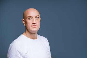 emotional portrait of an adult bald man in a white T-shirt on a gray background close-up.