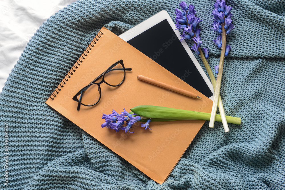 Notebook with flowers, eyeglasses and tablet computer on knitted plaid