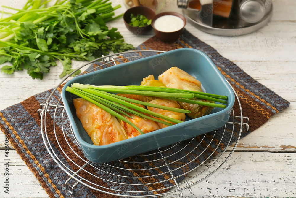 Baking dish with tasty stuffed cabbage rolls on light wooden background