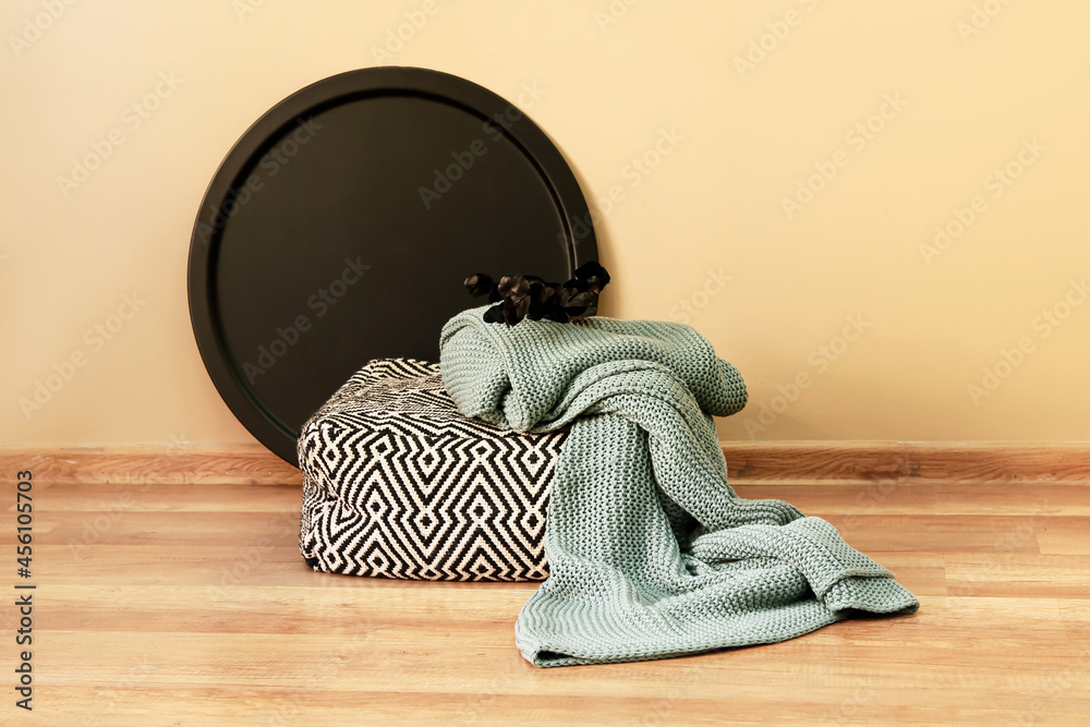 Small pouf, soft plaid and branch on floor near color wall