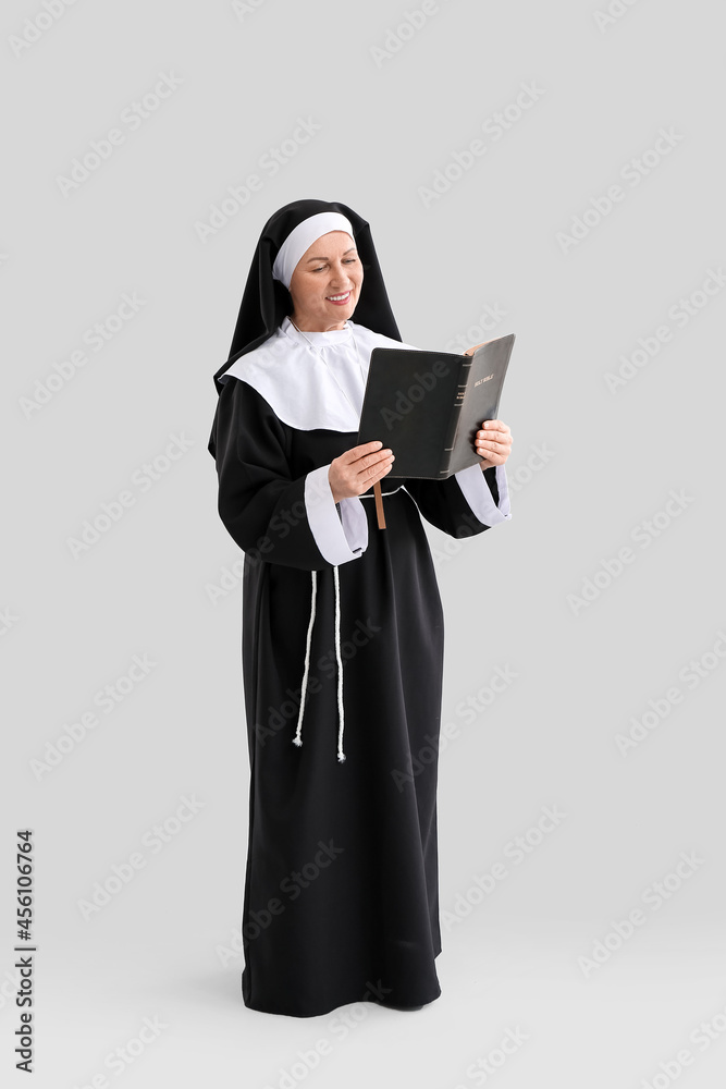Mature nun reading Holy Bible on light background