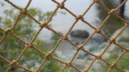 Close Up Of Rope Net Fence With Blurred Ocean In The Background.