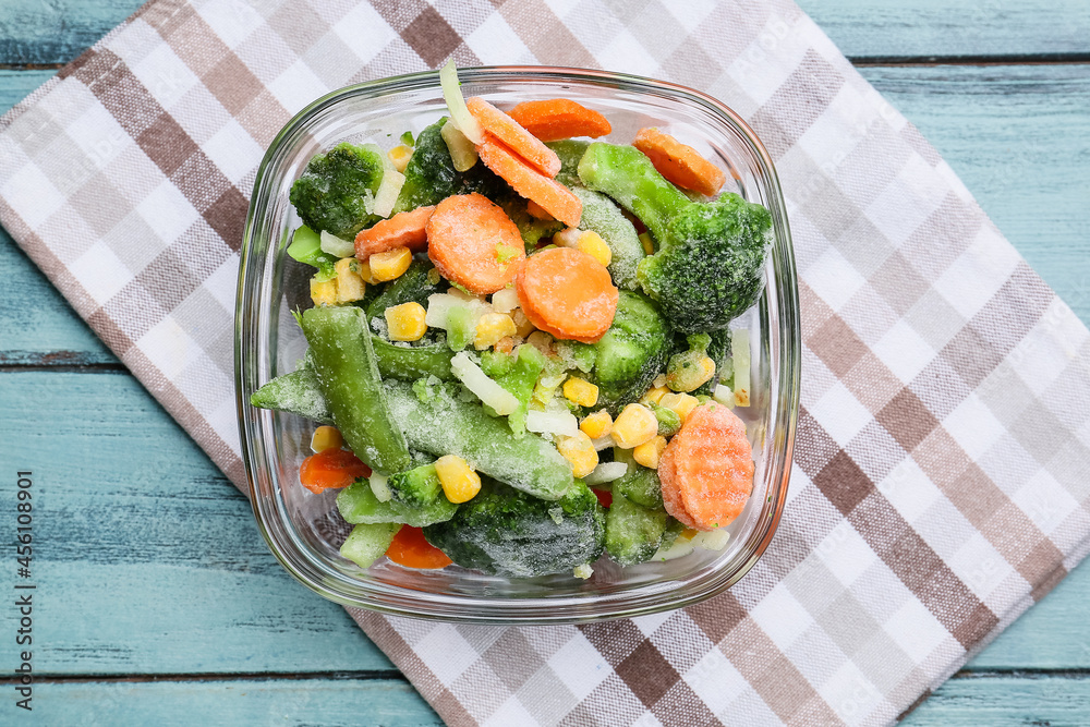 Bowl with different frozen vegetables on color wooden background