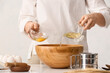 Female chef adding ingredients for dough in bowl on kitchen table, closeup