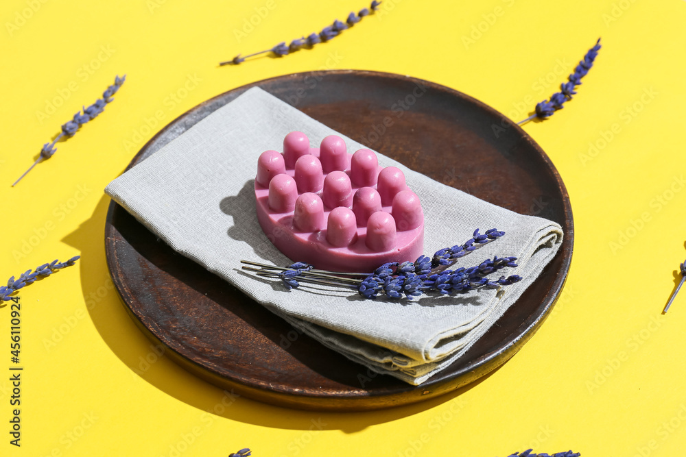 Plate with massage soap bar and flowers on color background