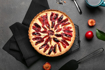 Composition with tasty plum pie and cup of tea on dark background