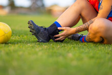 Detail Of Football Player Sitting On Grass Adjusting Ankle Brace