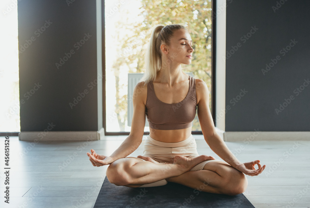 Portrait of young slim sportive woman in sportswear doing yoga exercise on sports mat at yoga meditation center. Concept of healthy lifestyle, wellbeing, mental health