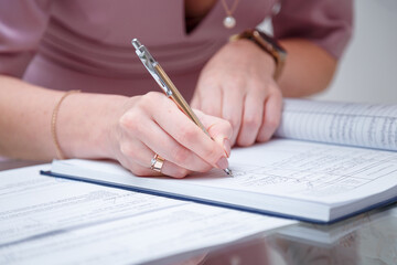 Close up shot of bride signing up the festive wedding document of marriage registration, only hands with ring, pen visible.