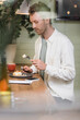 © LIGHTFIELD STUDIOS - curly man holding fork with piece of lemon tart near smartphone and cup in cafe