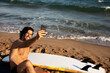 Portrait of handsome surfer with his surfboard. Young man taking selfie photo at the beach.