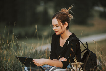 Poster - Shallow focus shot of a Bosnian Caucasian woman with a laptop in her lap outdoors in a field