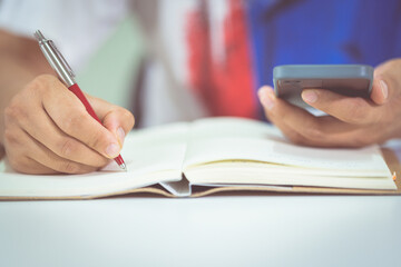 Sticker - Closeup shot of a student writing in a notebook while reading from a phone