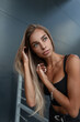© alones - Beauty portrait of fashion sexual caucasian woman model with pretty face in black tank top with silver bracelet near a black metal building in the city