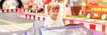 Little Happy Four Years Old Kid Boy Fun Riding An Small Electric Cars On Sport Ground In A Playground For Entertainments. Children Riding In The Toy Auto In An Amusement Park. Banner. Flare