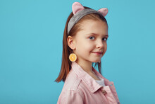 Portrait Of Caucasian Little Girl In Pink Jacket And Kitty Ears Headband, Smiling And Posing Adorable Against Blue Studio Background