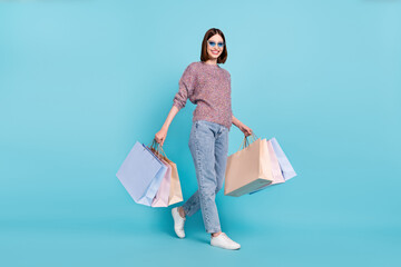Wall Mural - Photo of traveler lady walk carry store bags wear sunglass sweater jeans shoes isolated blue color background