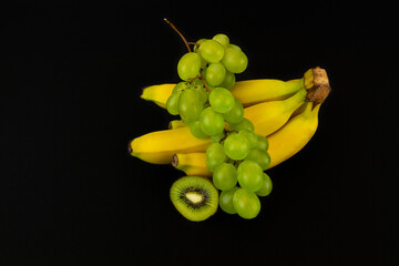 Poster - Closeup shot of fresh slices of kiwi, bananas, and green grapes isolated on a dark background