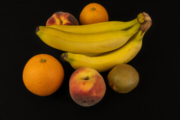 Poster - Closeup shot of ripe banana, kiwi, peaches, and oranges isolated on a black background